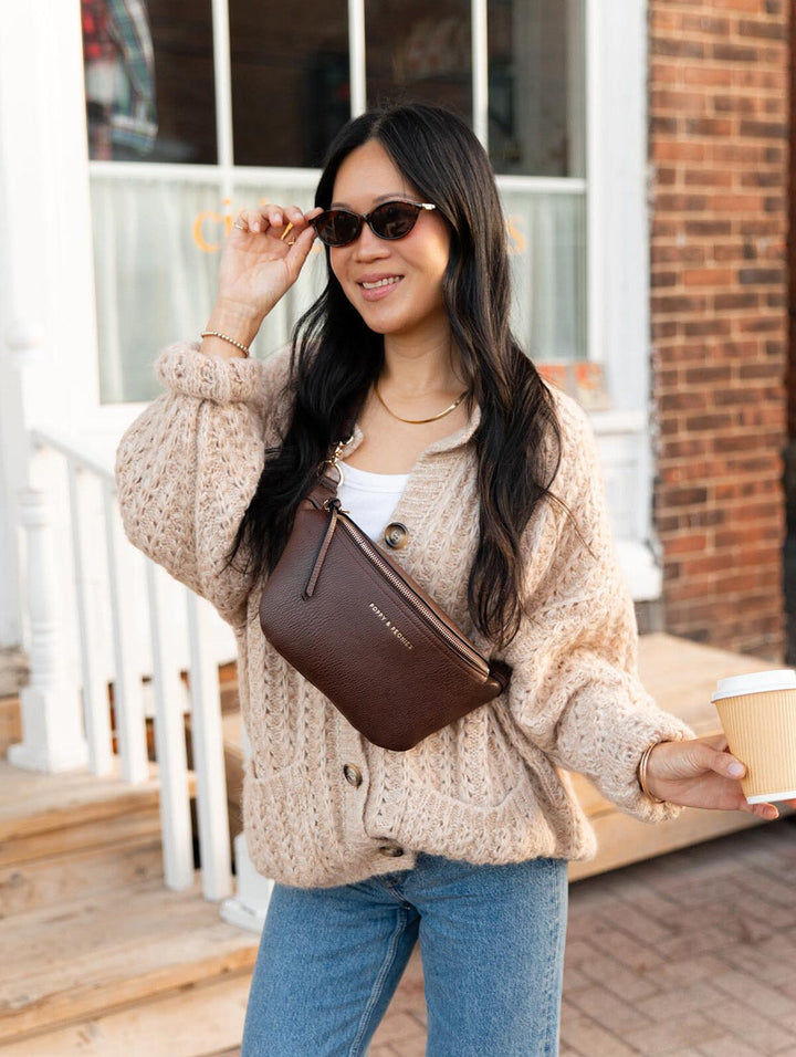 Poppy & Peonies The Sidekick in Espresso close-up lifestyle view, worn crossbody over a chunky cream cardigan as a woman smiles while holding a takeaway coffee.