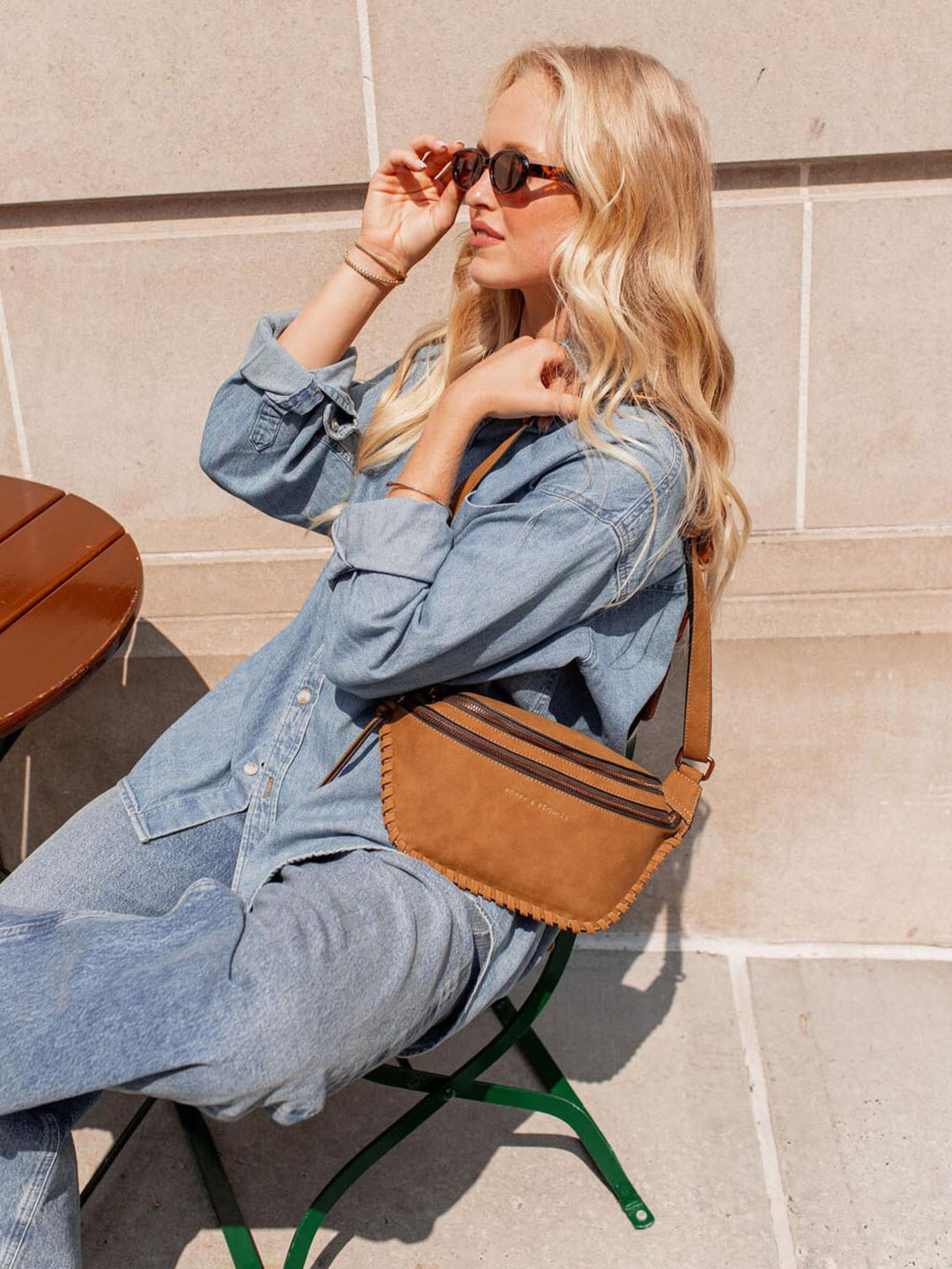 Woman sitting outdoors wearing a denim outfit and cognac coloured vegan suede belt bag.