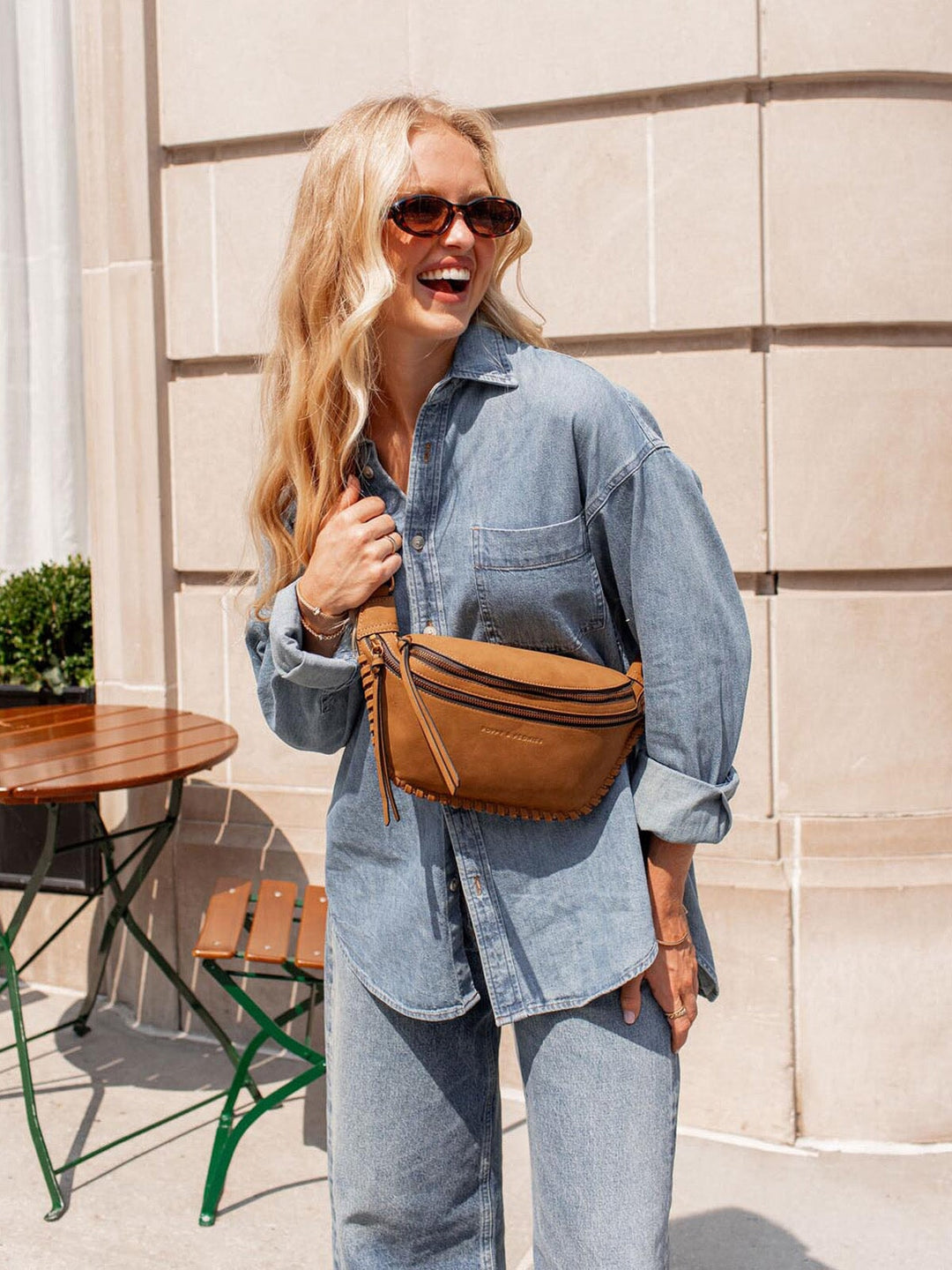Woman wearing a denim outfit with a cognac coloured vegan suede belt bag, standing outdoors.