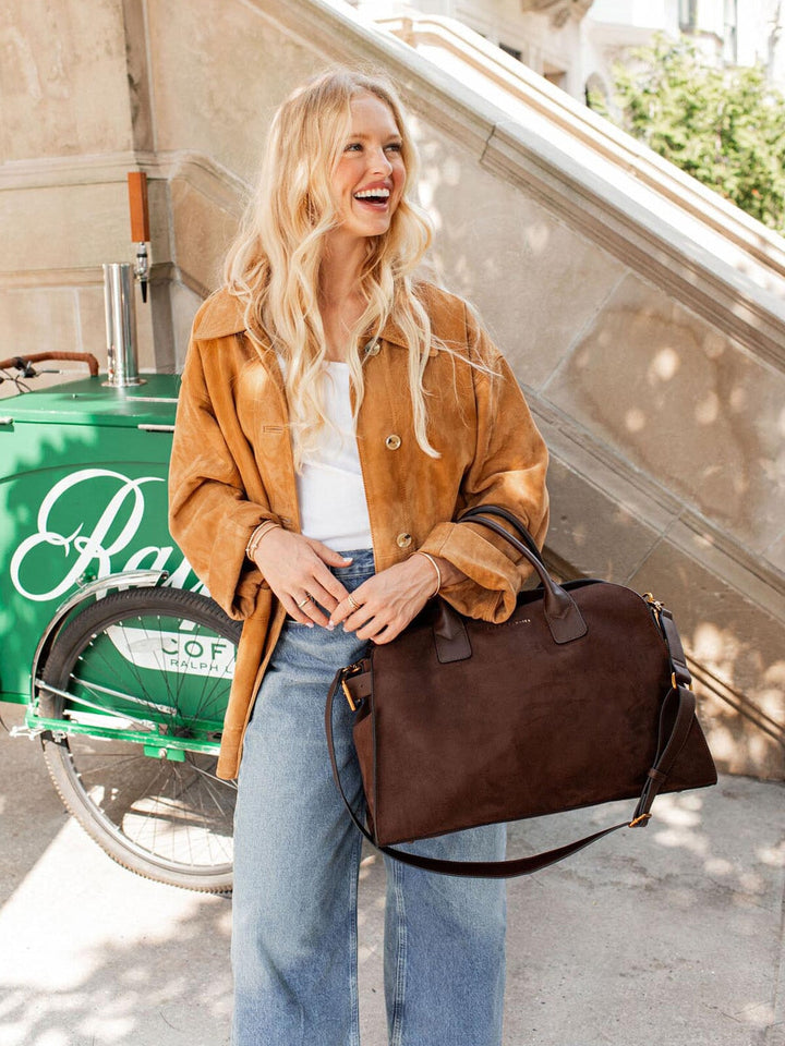 Woman holding a brown vegan suede bag in an urban setting.