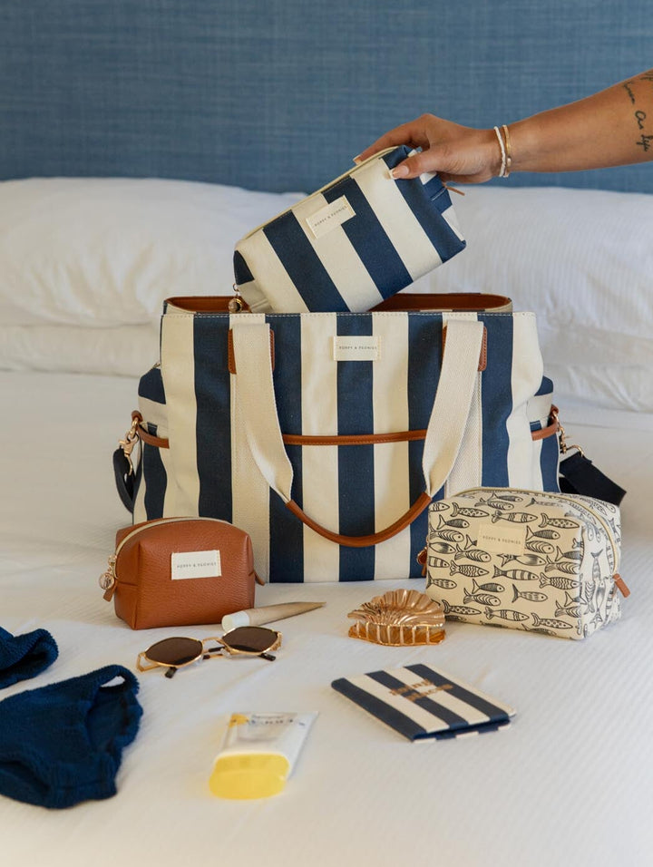 Person organizing striped bags and travel items on a bed