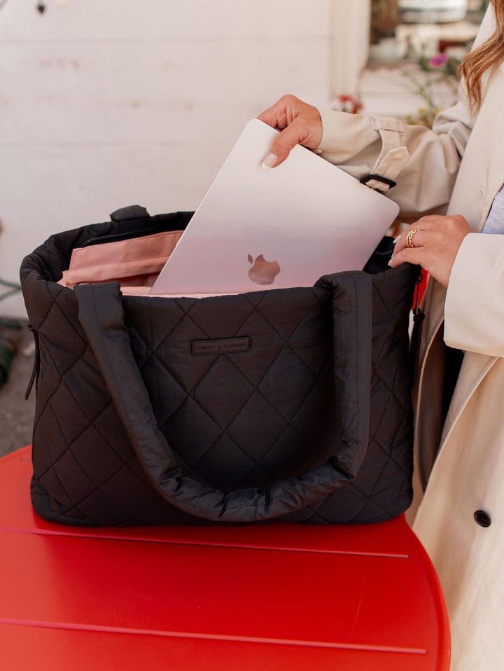 Person placing a laptop into a black quilted bag on a red surface.