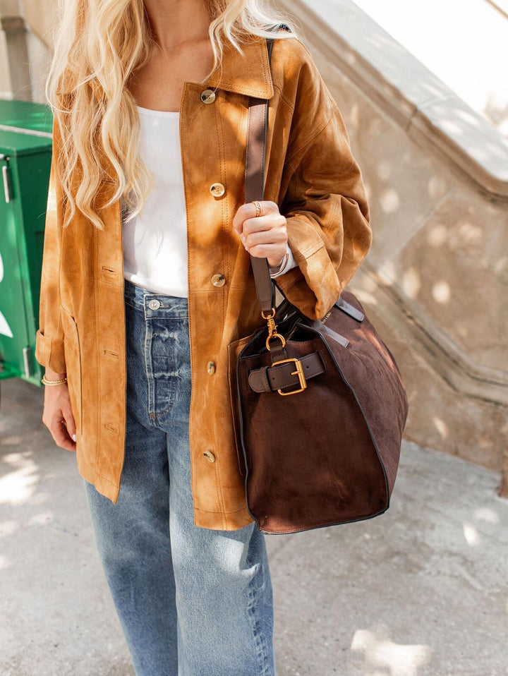 Person wearing a brown suede jacket and holding a brown vegan suede bag.