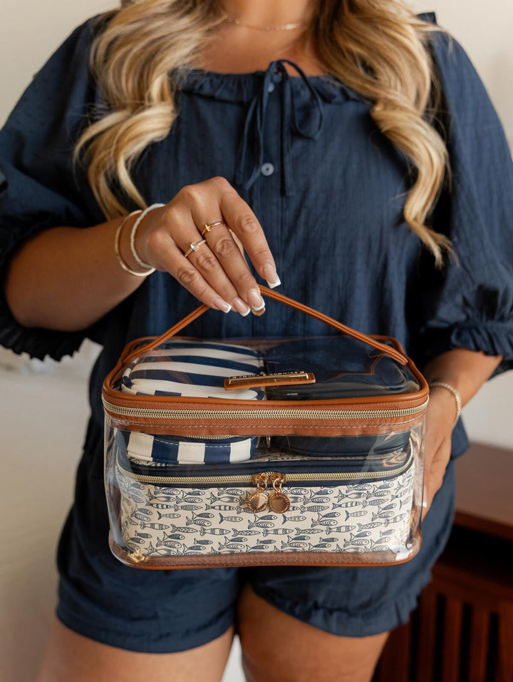 Woman holding a clear cosmetic bag with a brown handle and patterned pouches inside