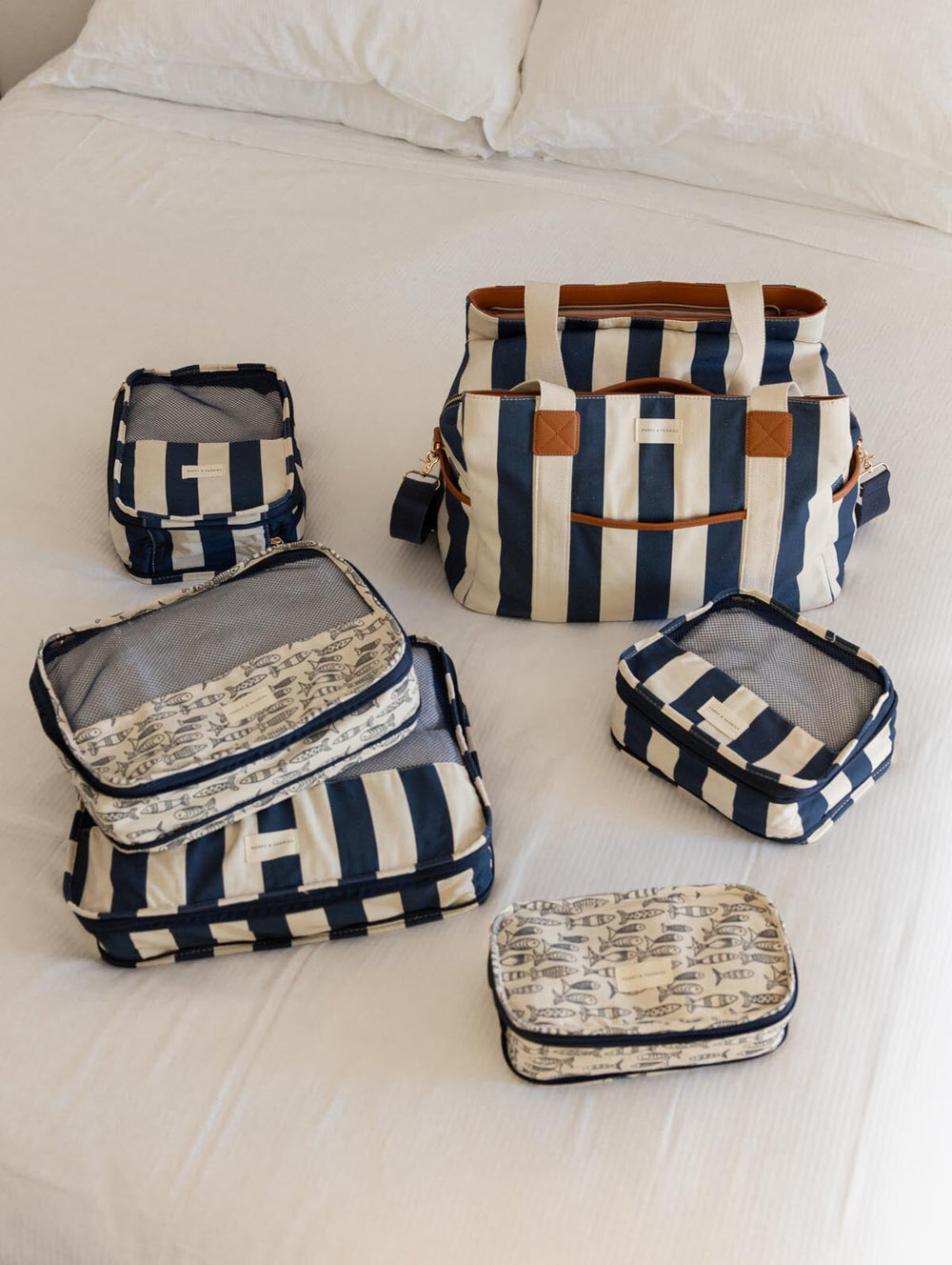 Set of navy and white striped packing cubes and a striped tote bag on a bed