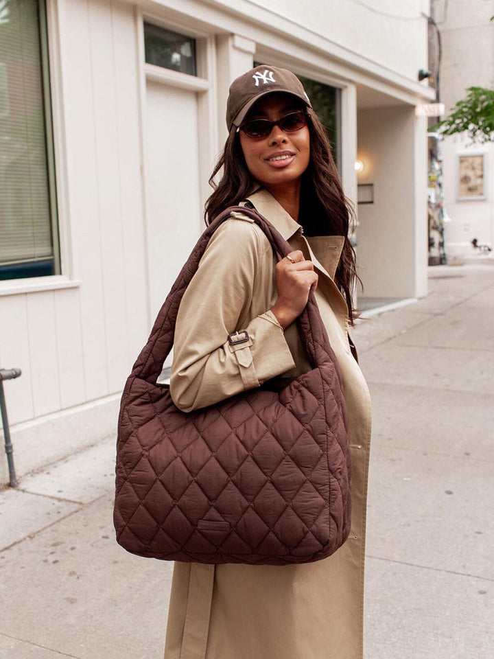 Woman holding a quilted brown hobo bag on a city street