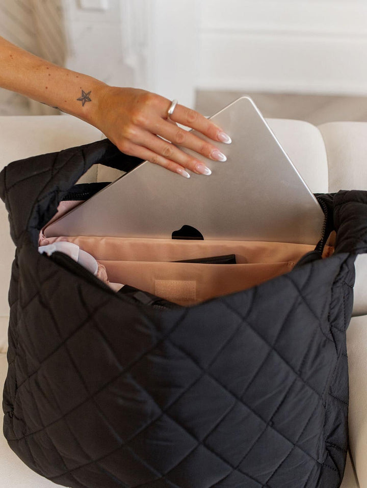 Person placing a laptop into a quilted black bag.