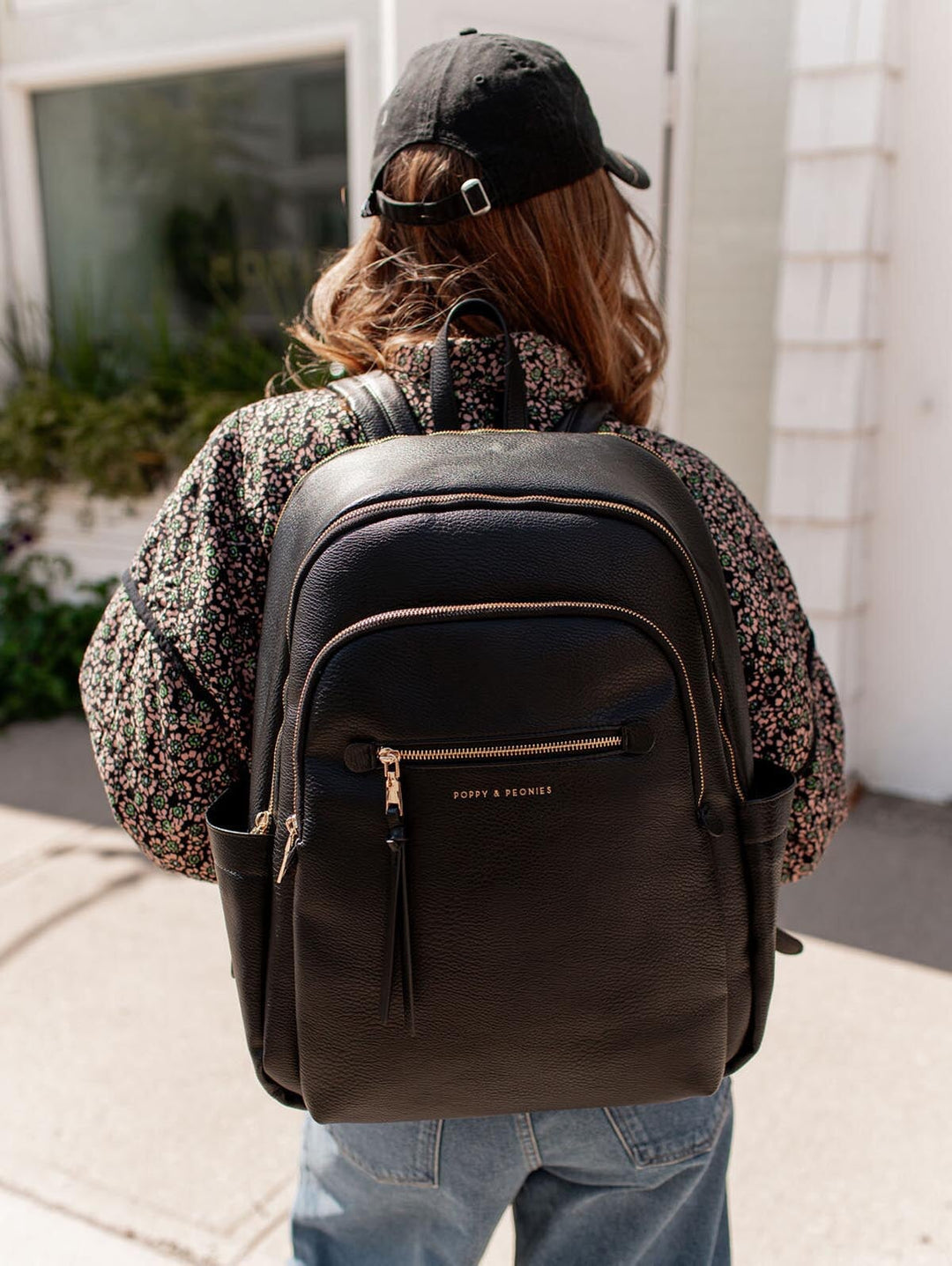 Person wearing a black backpack with Poppy & Peonies branding, standing outdoors.