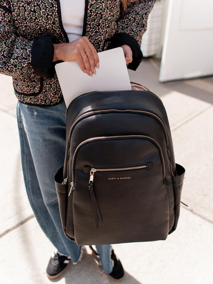 Person holding a black backpack with a laptop, wearing a patterned jacket and jeans.