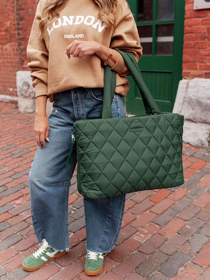 Person holding a green quilted bag on a brick street