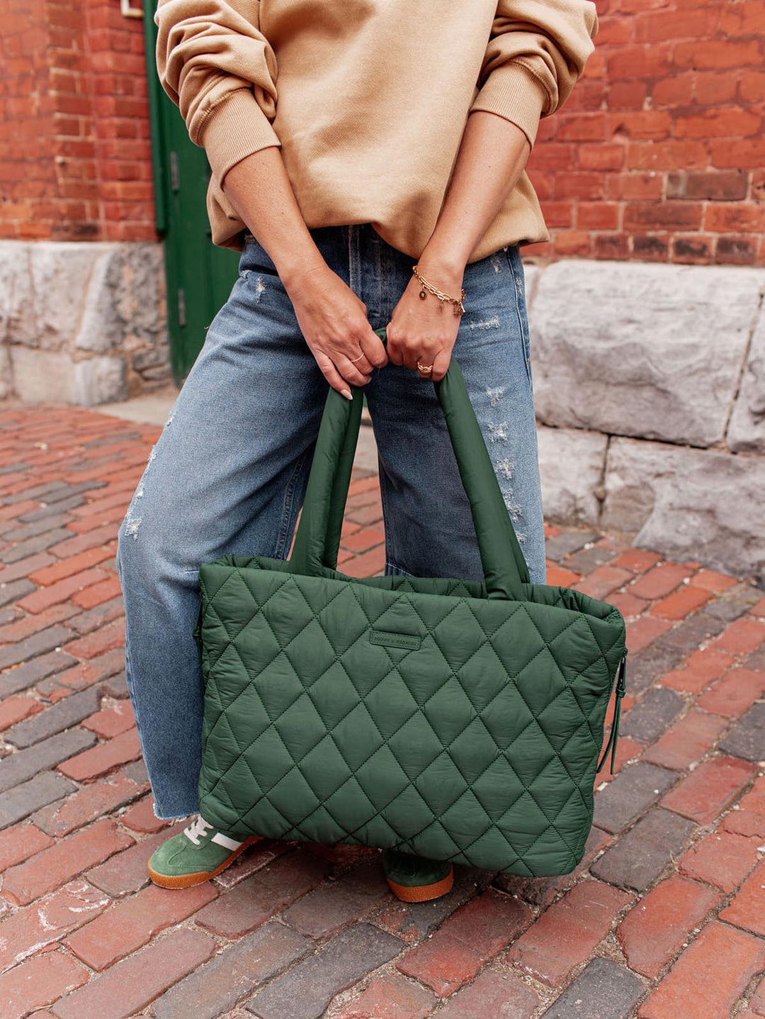 Person holding a green quilted tote bag on a brick sidewalk