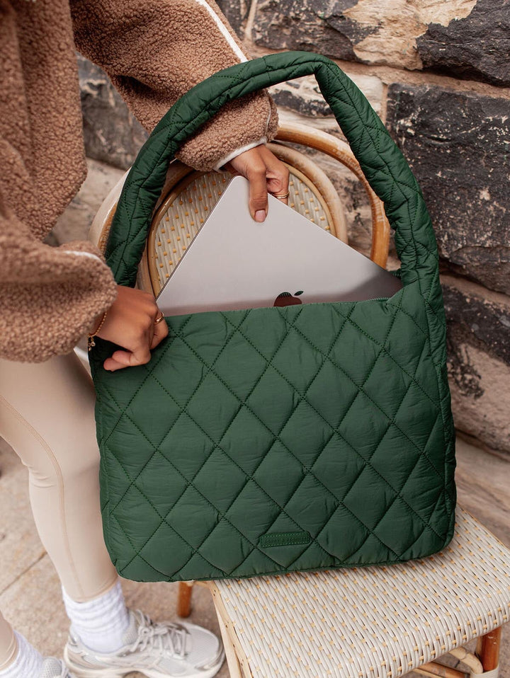 Person holding a green quilted handbag with a laptop inside