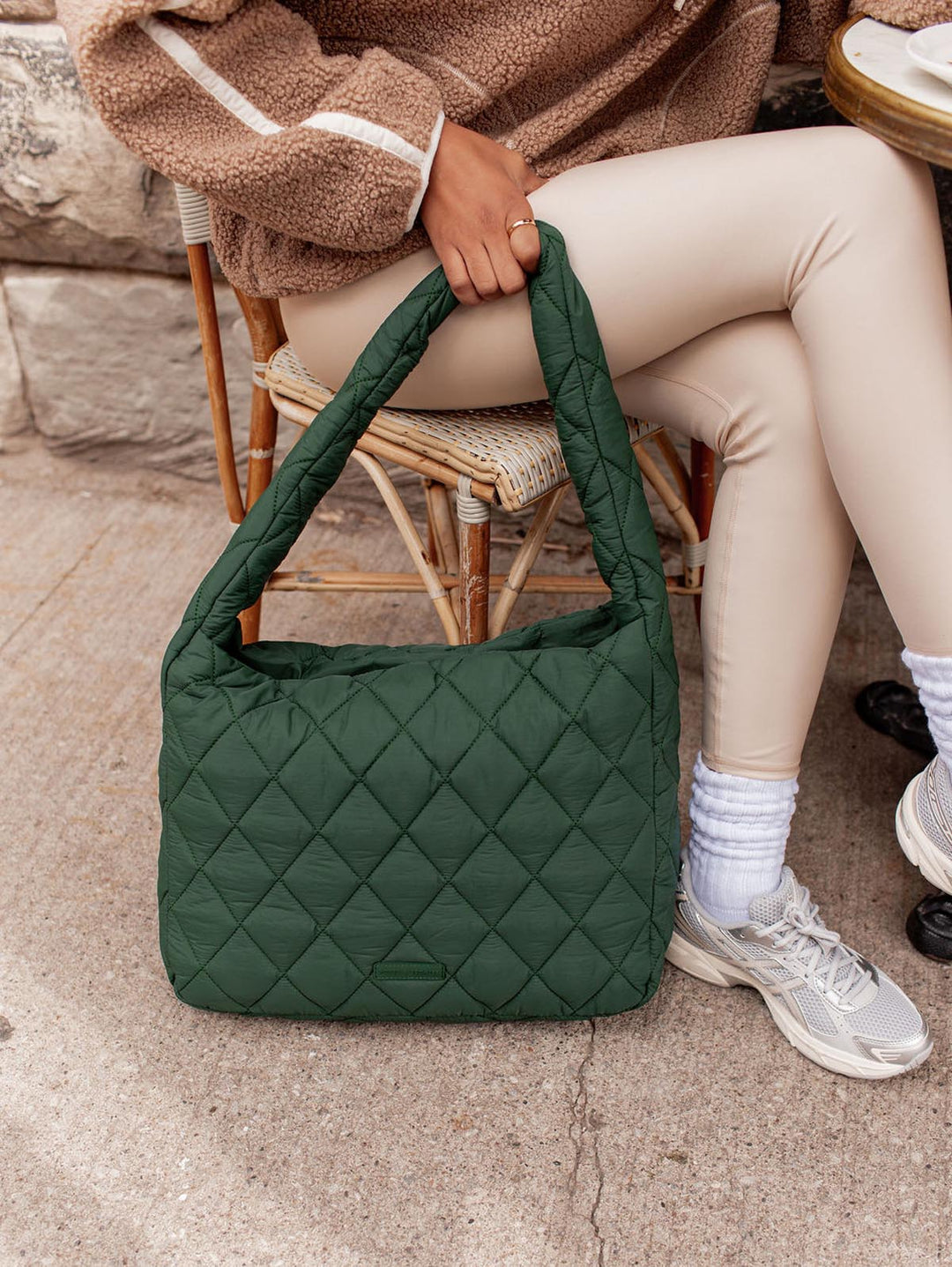 Green quilted hobo bag held by a person sitting on a chair.