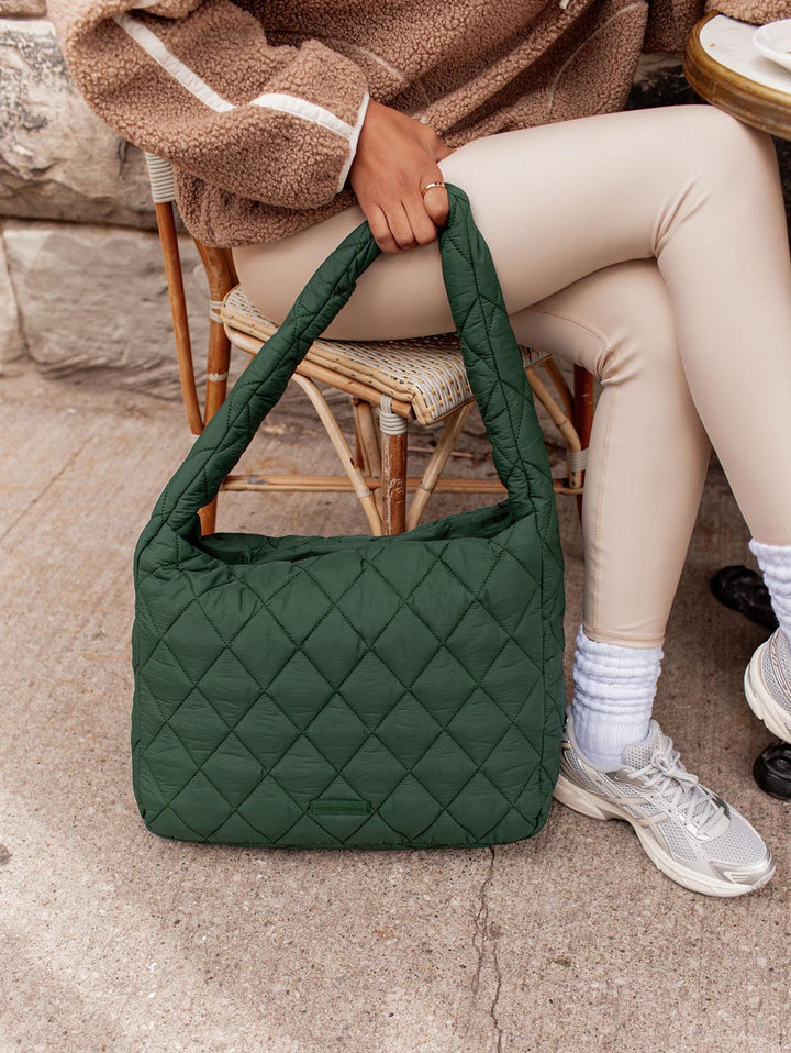 Green quilted hobo bag held by a person sitting on a chair.