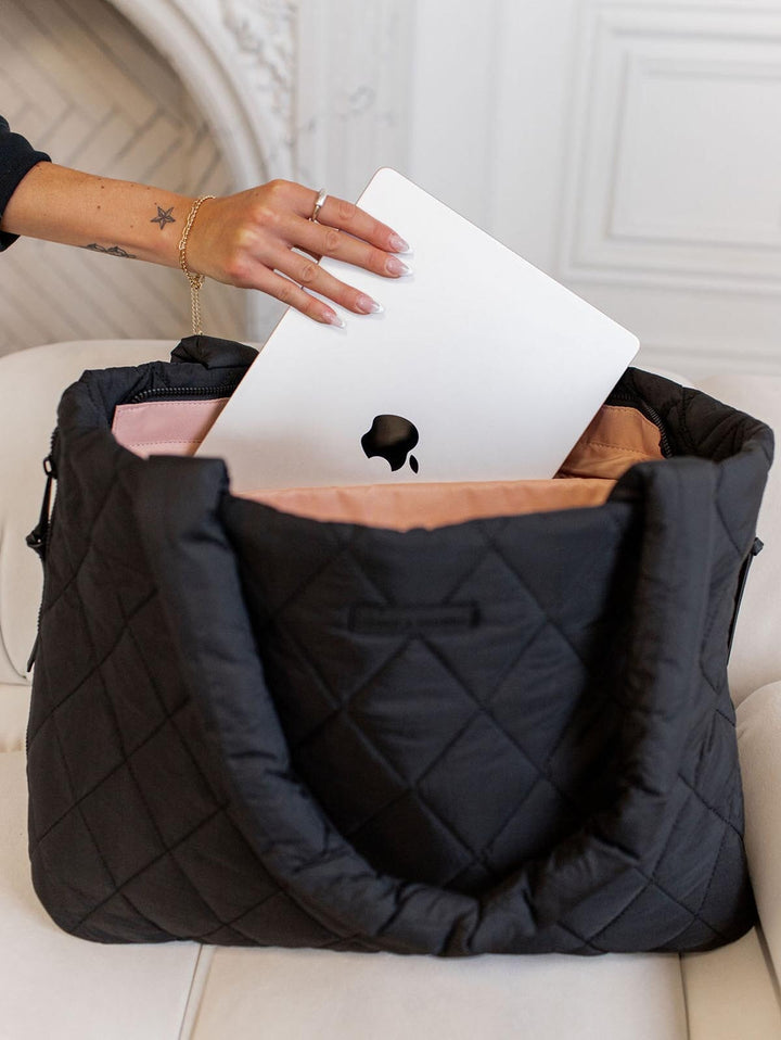 Person placing a MacBook into a black quilted bag on a white surface