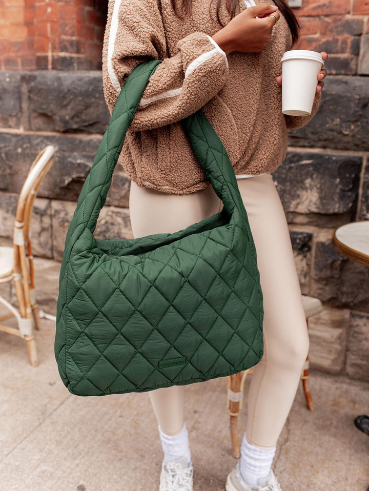 Person holding a green quilted handbag with a stone wall background