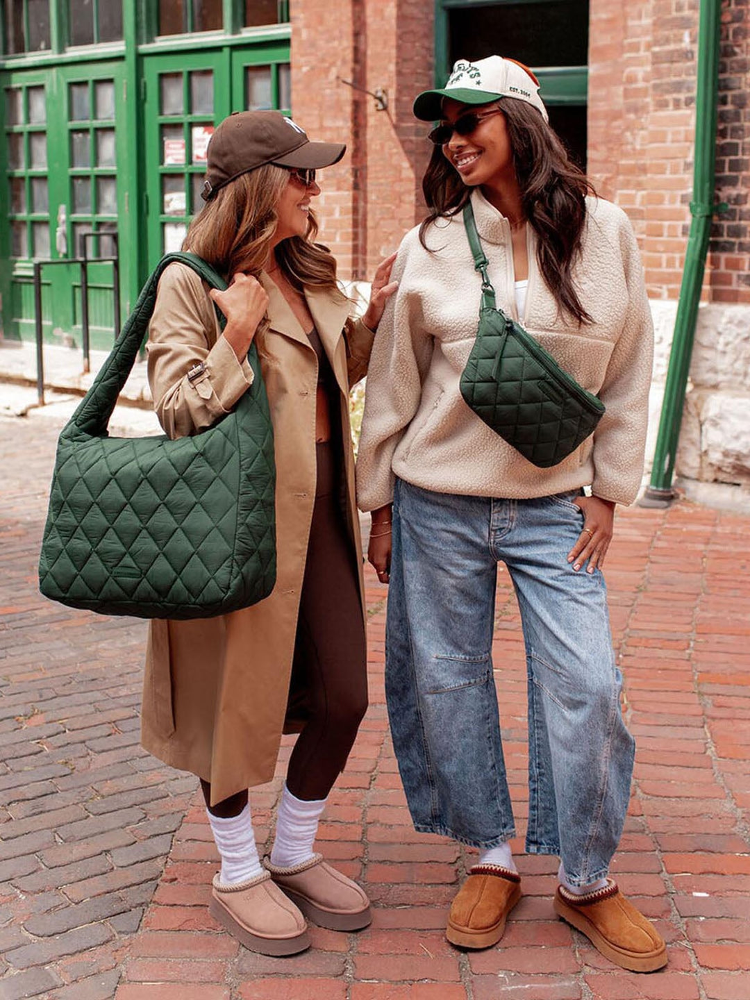 Two women walking on a brick sidewalk, each carrying a green quilted bag.