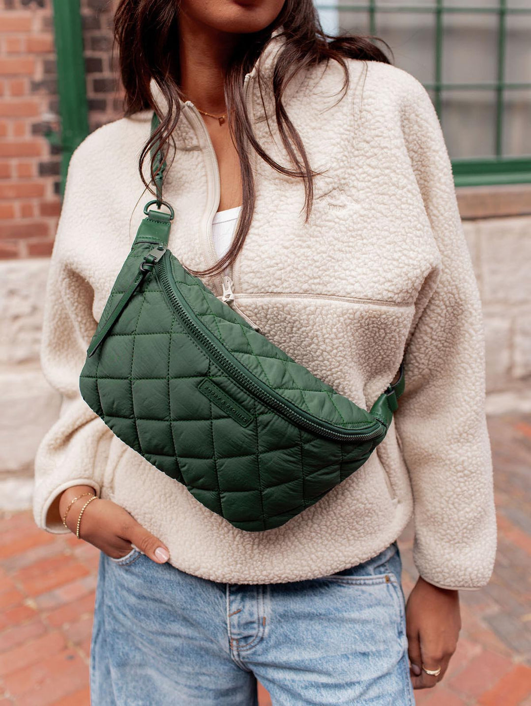Person wearing a green quilted crossbody bag with a neutral-colored sweater and jeans.