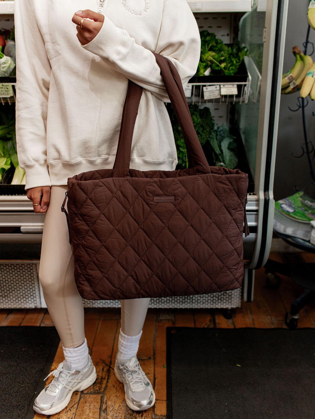 Person holding a brown quilted tote bag in a grocery store.