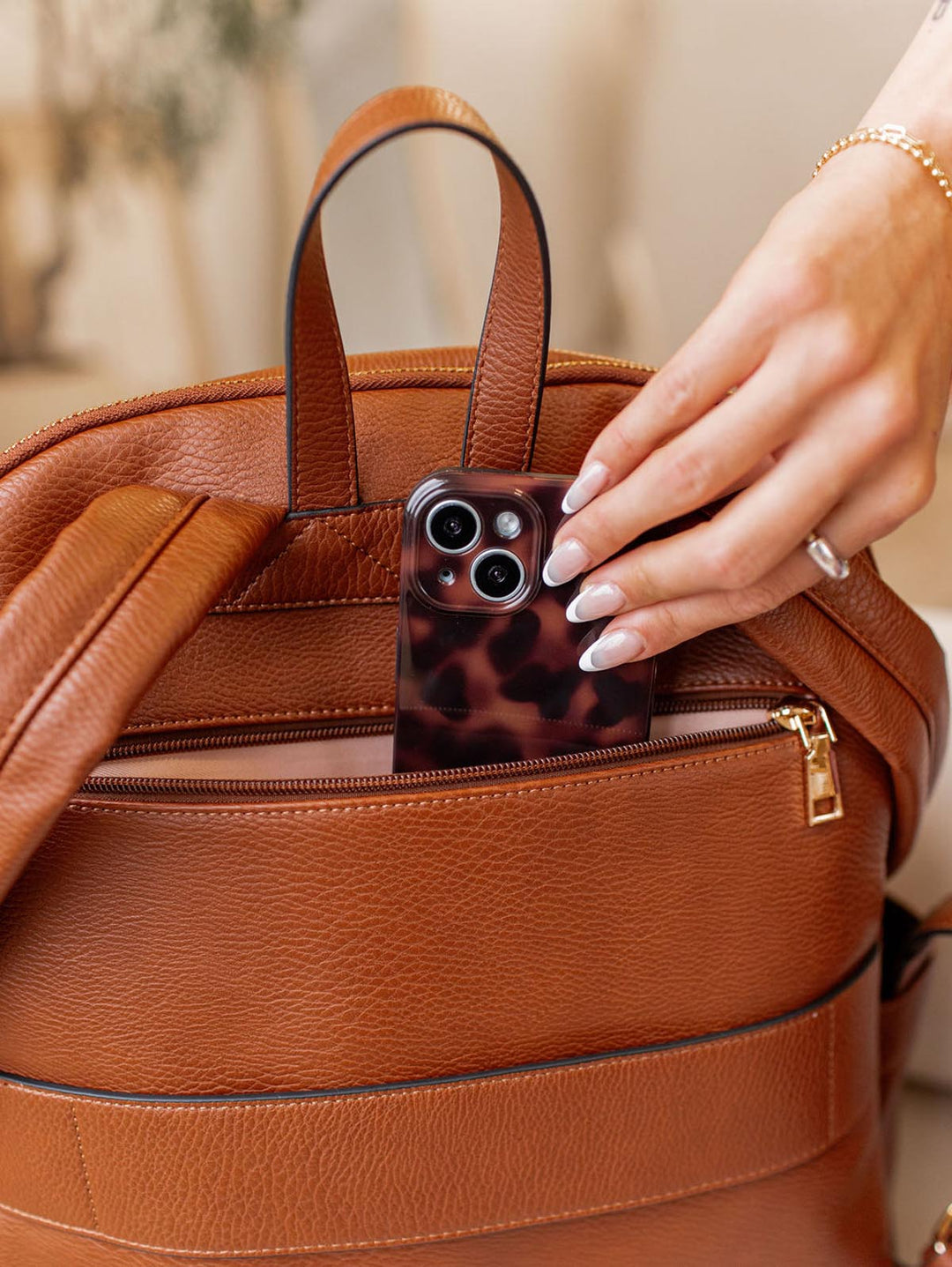 Person placing a phone with a leopard print case into a brown vegan leather backpack.