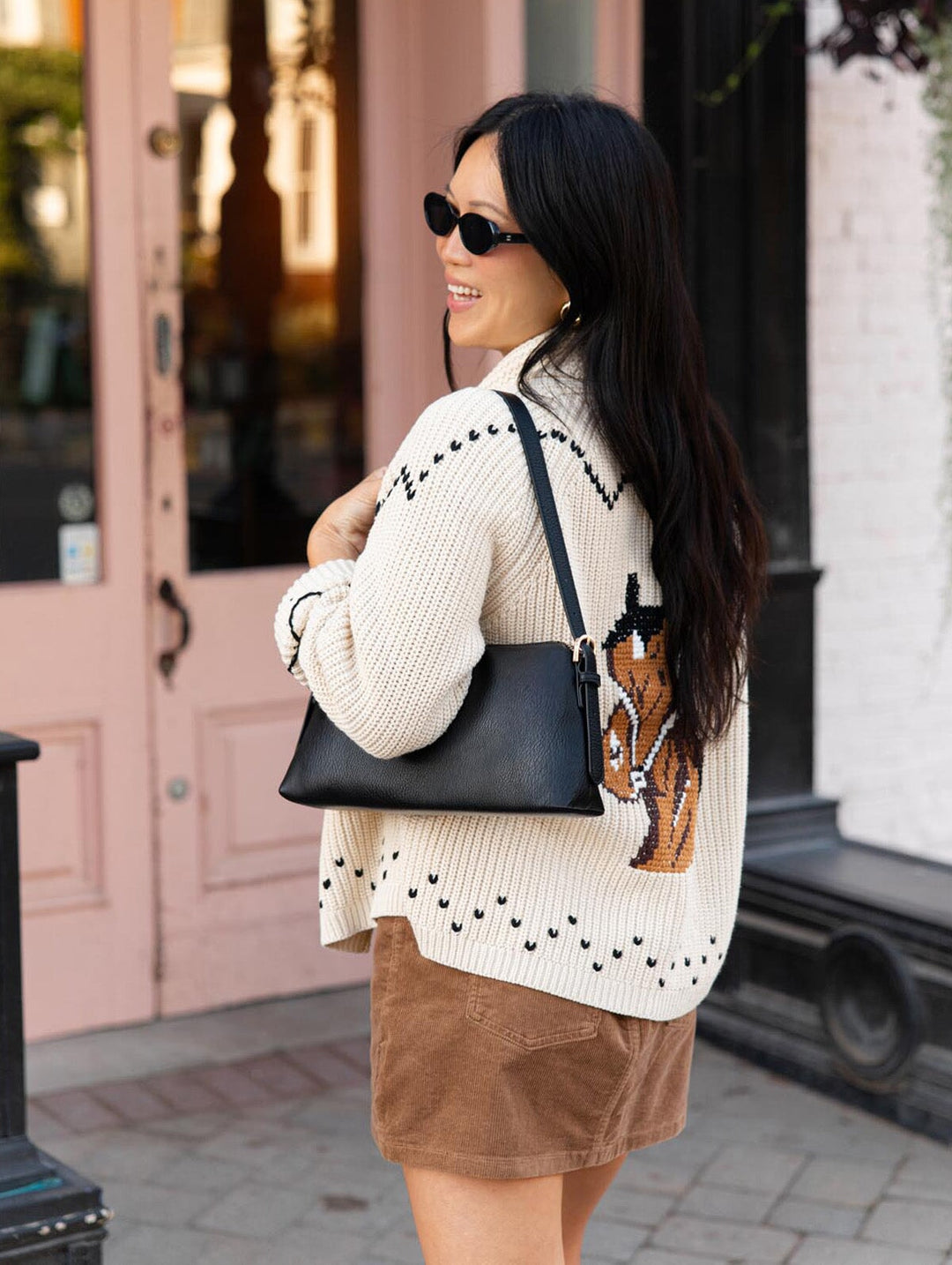 Poppy & Peonies The Soho Shoulder Bag in Black shown from the side and back, worn over the shoulder with a cream patterned cardigan and brown skirt.