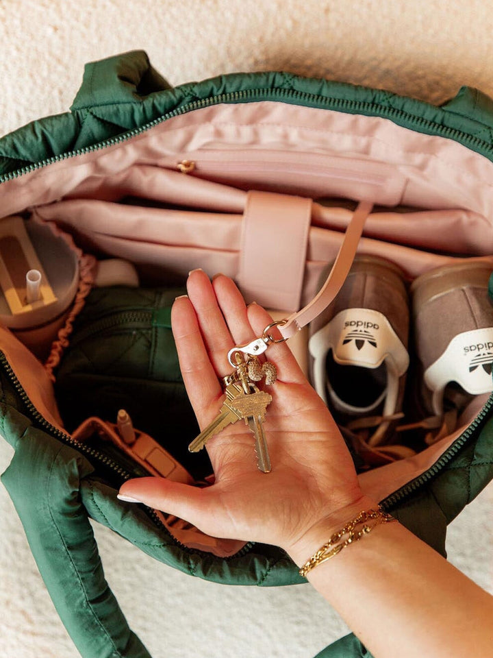 Hand holding keys over an open green quilted tote bag with a beige interior.