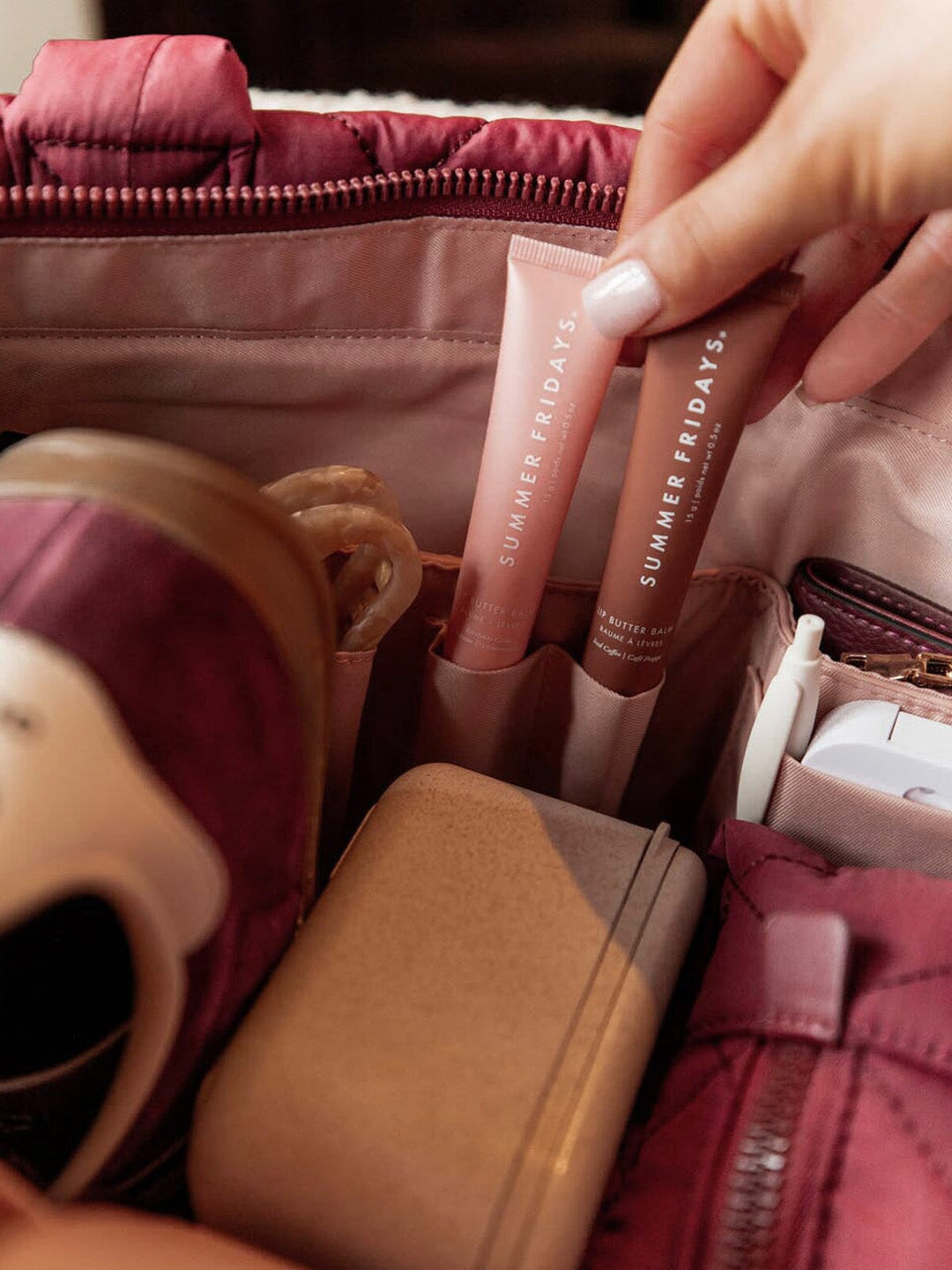 Person holding two lip products with 'Summer Fridays' branding inside a berry coloured quilted bag.