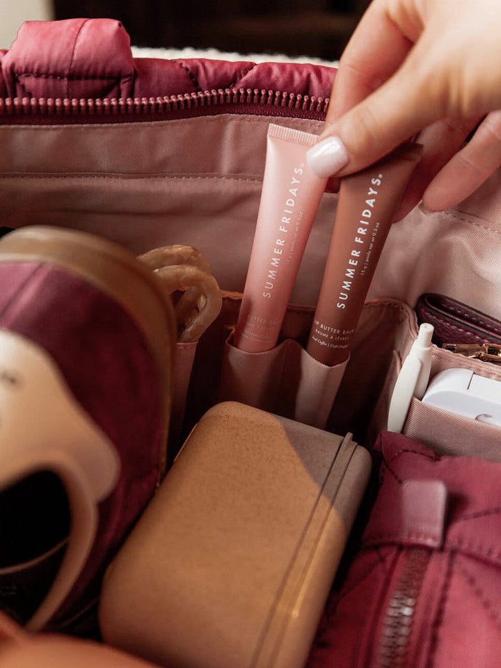 Person holding two lip products with 'Summer Fridays' branding inside a berry coloured quilted bag.
