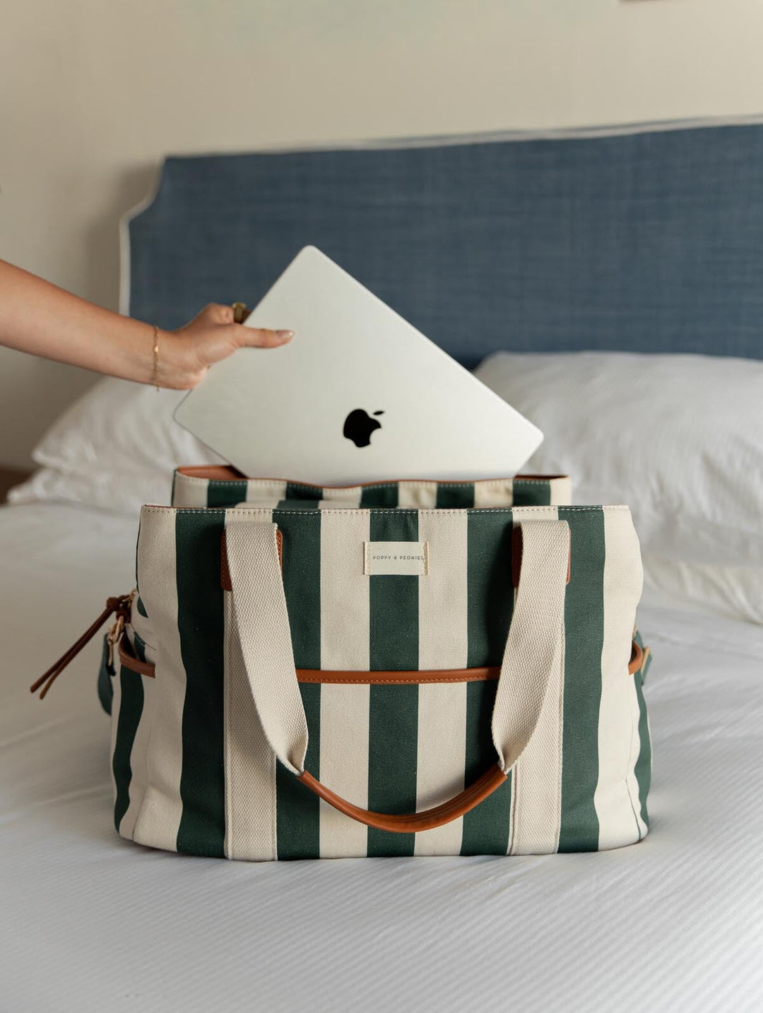 Person placing a laptop into a green and white striped bag on a bed.