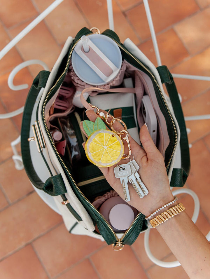 Hand holding a keychain with a lemon design over an open green and white bag.