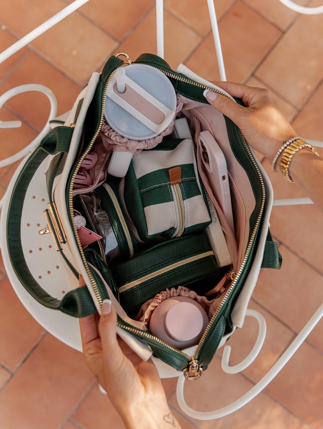 Open handbag with various items including a phone, matching cosmetic bags, and water bottles on a tiled floor.