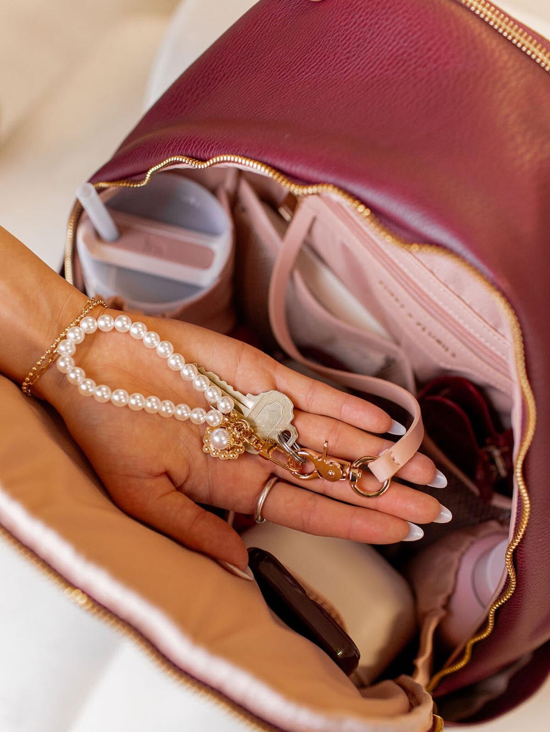Hand holding a pearl keychain over a berry coloured backpack