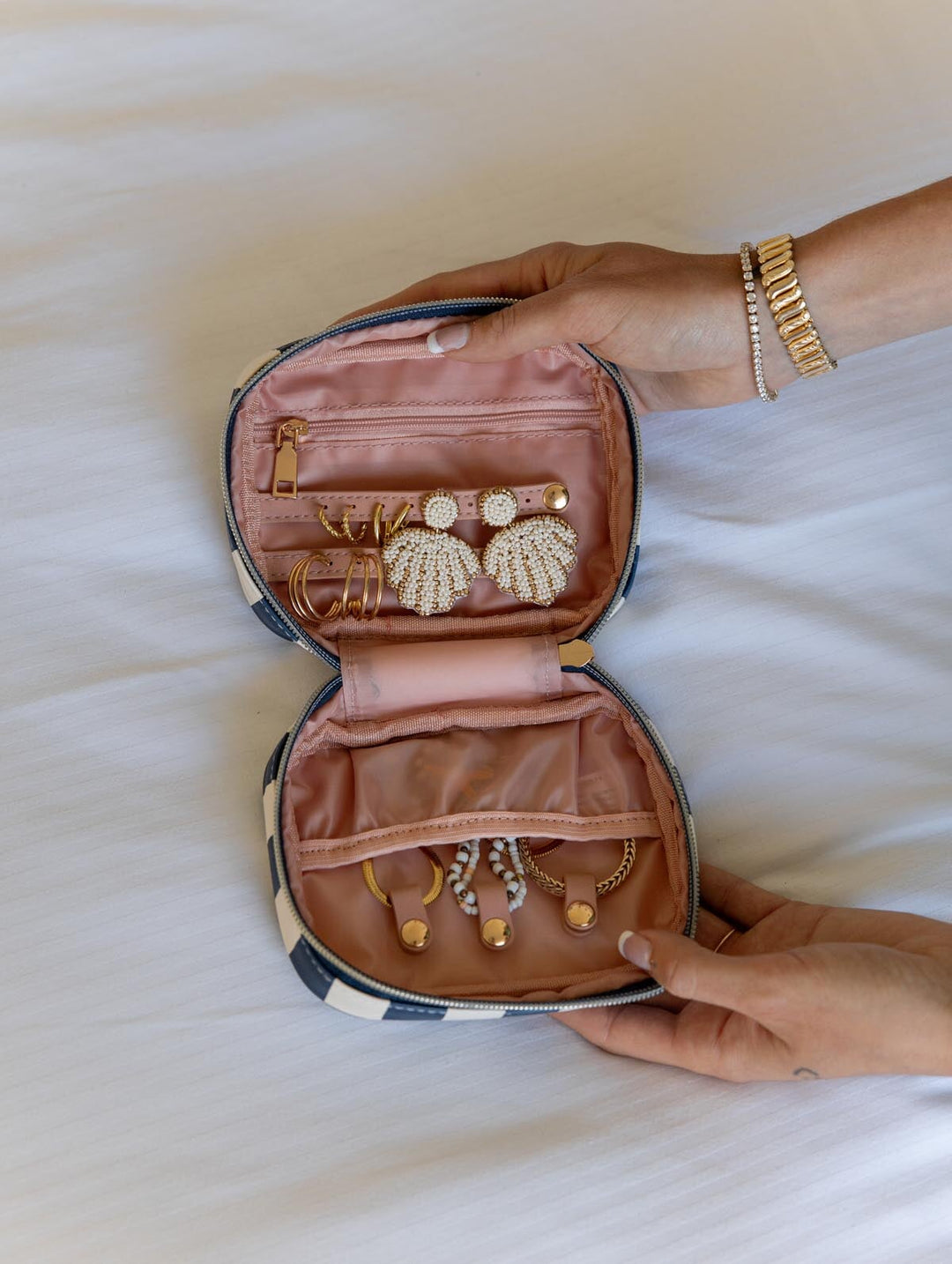 Small jewelry case with earrings and bracelets held by a hand on a light background