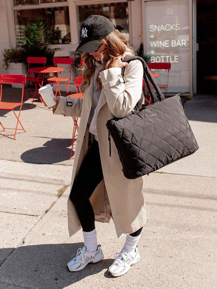 Person holding a black quilted bag on a sidewalk with a casual outfit.
