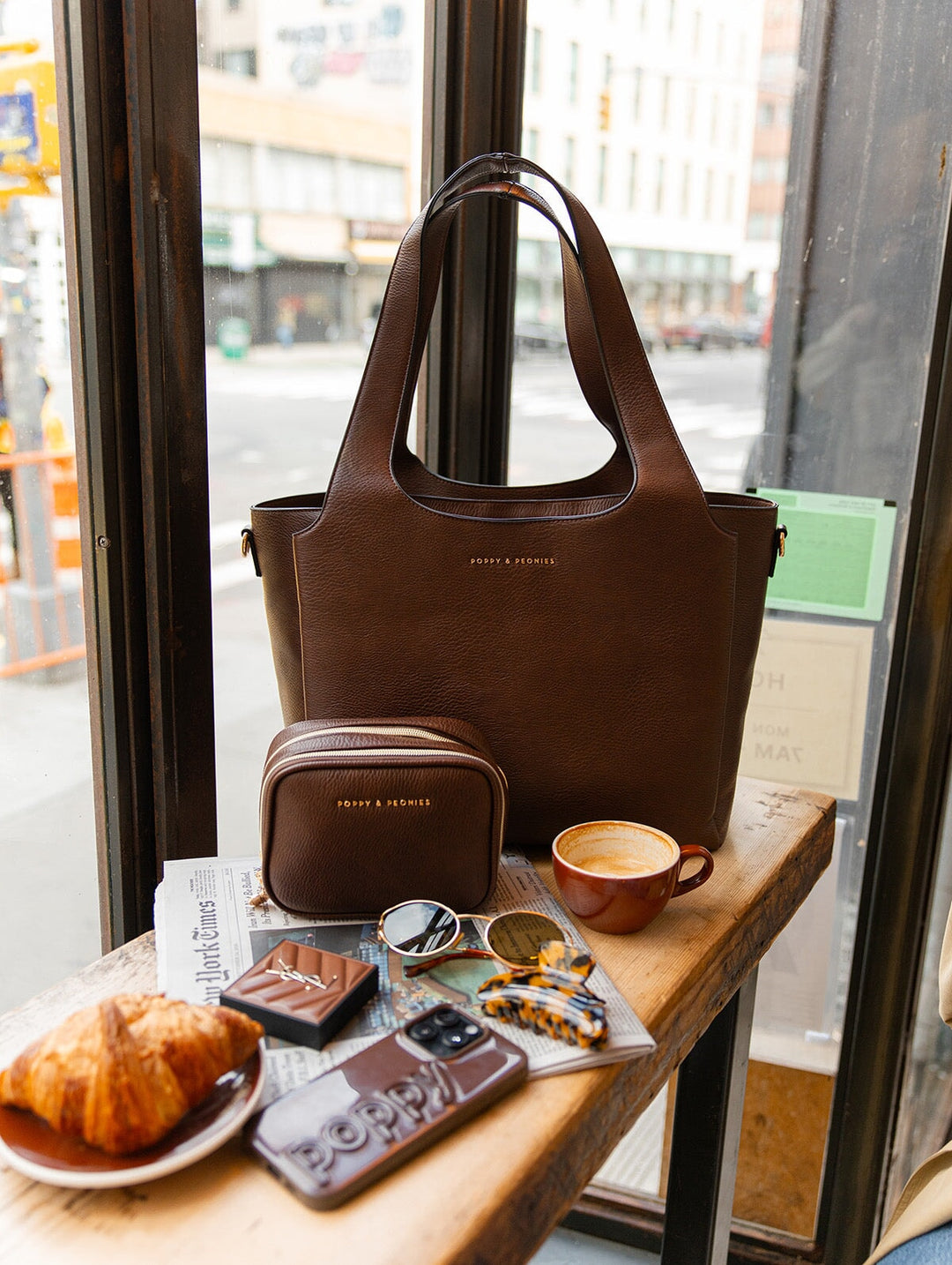 Poppy & Peonies The Companion Tote and Pretty Connected Case in Espresso displayed together on a café counter, highlighting the rich brown vegan leather, structured silhouettes and signature gold-tone logos.