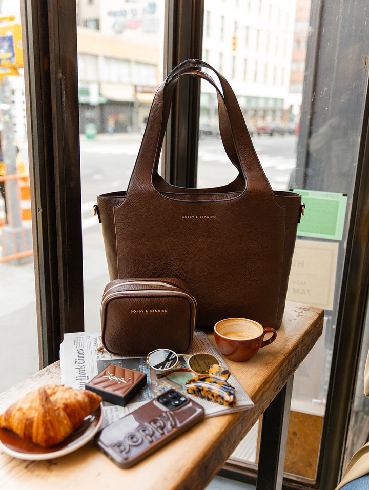 Poppy & Peonies The Companion Tote and Pretty Connected Case in Espresso displayed together on a café counter, highlighting the rich brown vegan leather, structured silhouettes and signature gold-tone logos.