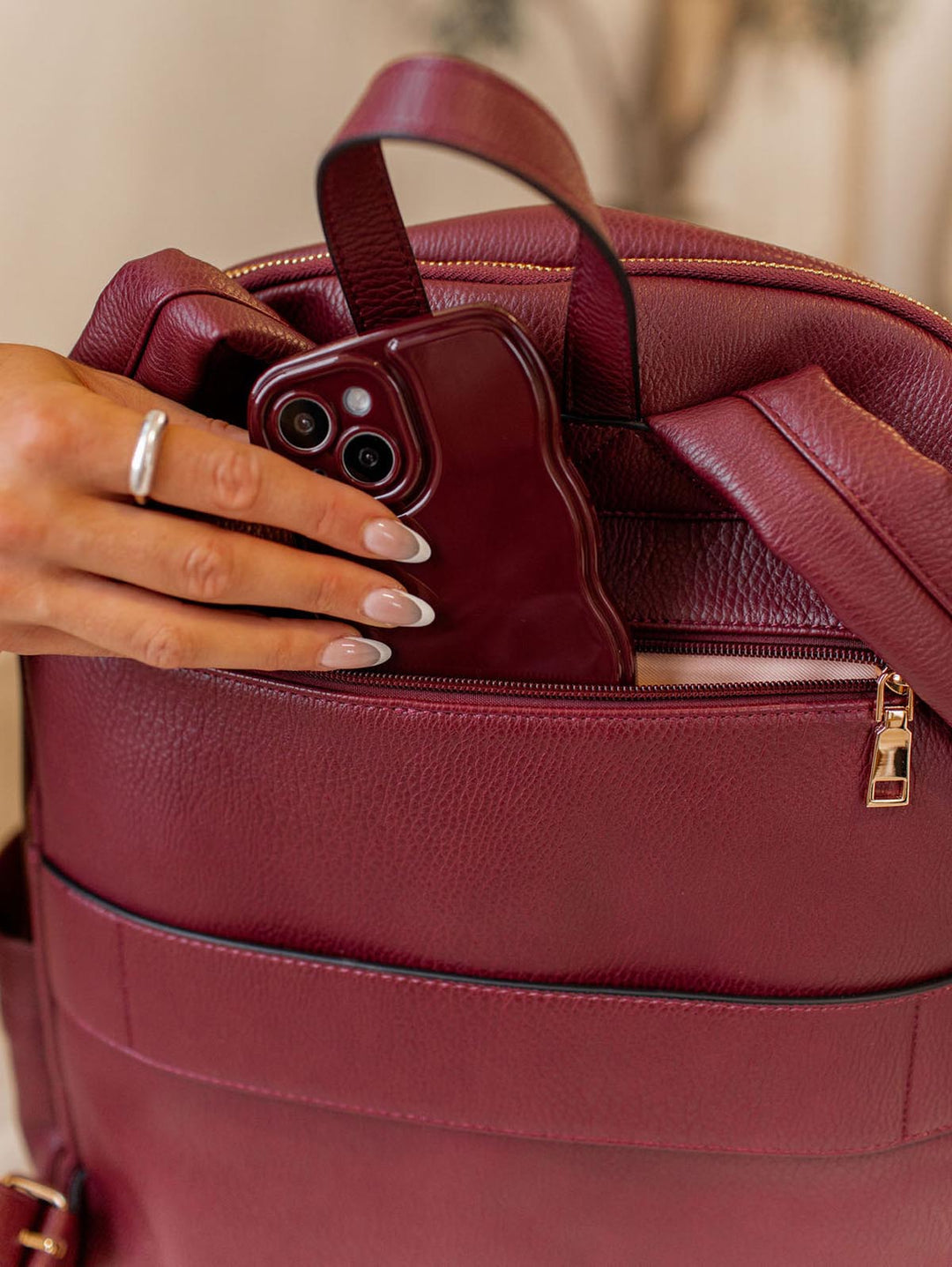 Berry coloured vegan leather backpack with a phone being placed inside