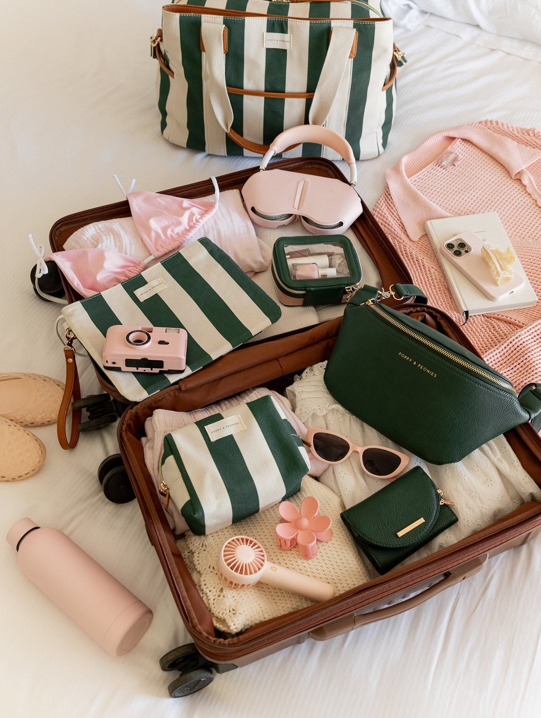 Open suitcase with travel items including a striped bag, sunglasses, and clothes on a bed.