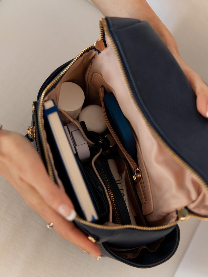 Hand holding a navy blue backpack with gold accents, open to reveal its contents