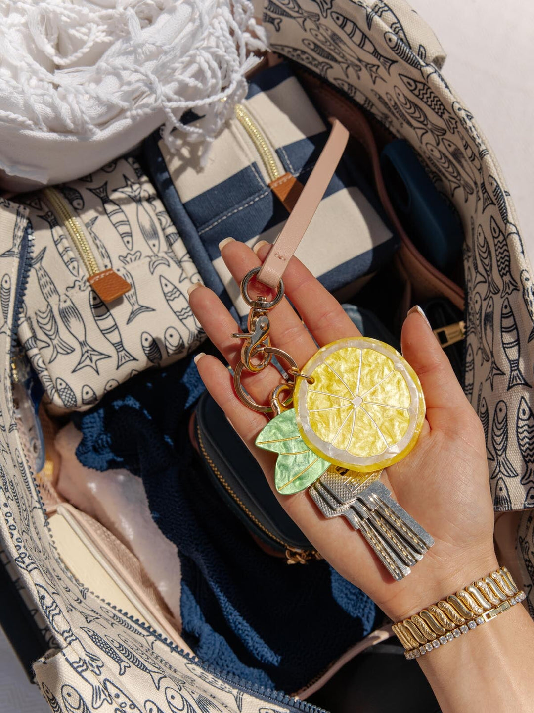 Hand holding a keychain with lemon and leaf design in front of an open bag.