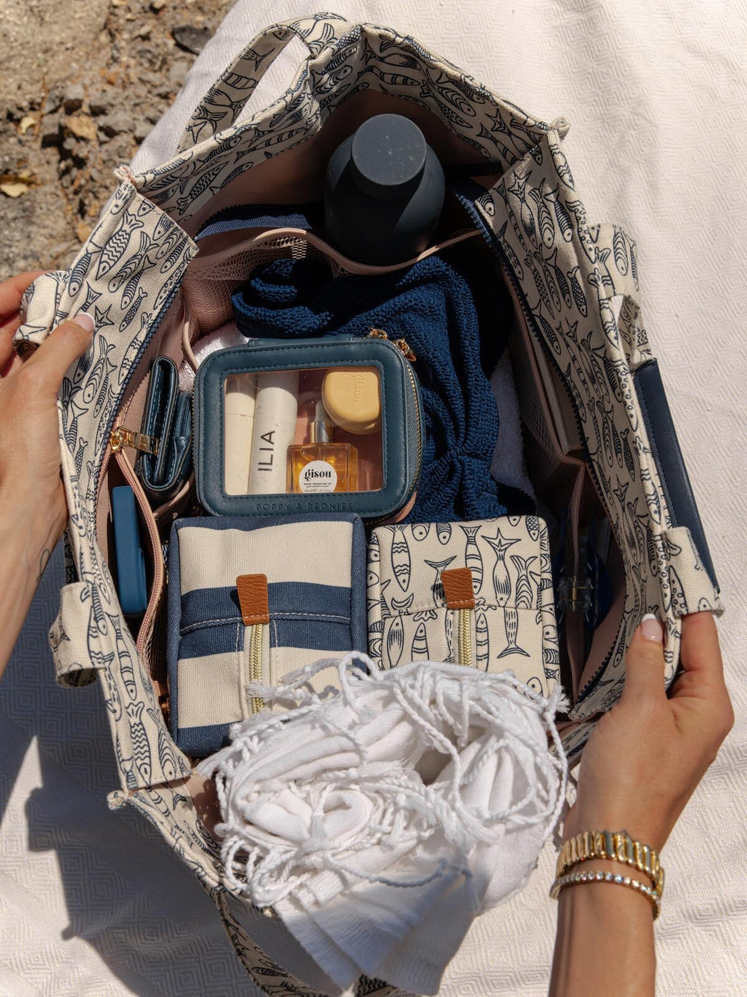 Open sardine printed tote bag with travel essentials including a bottle, towel, and toiletries.