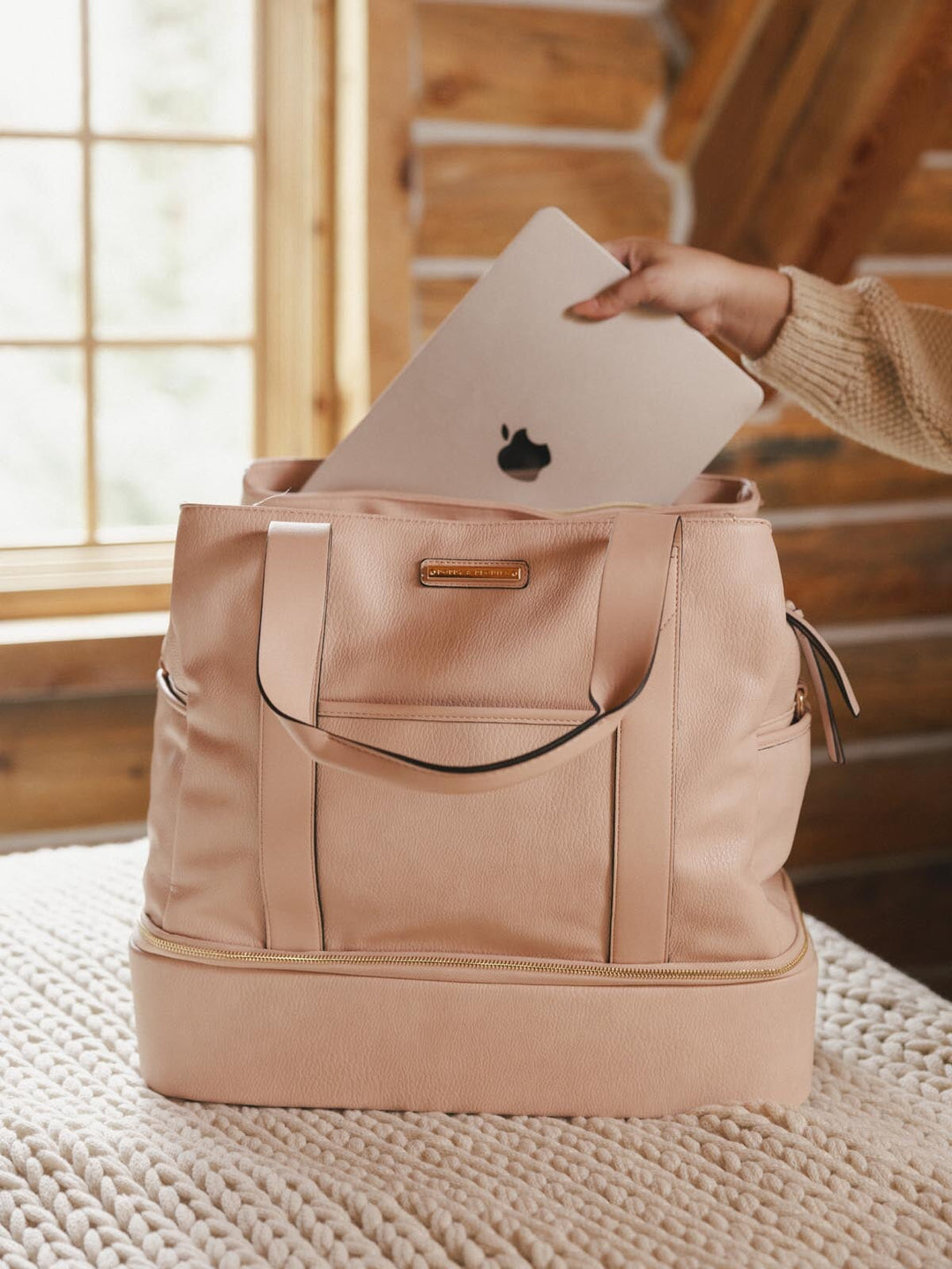 Hand placing an Apple laptop into a blush coloured vegan leather travel bag