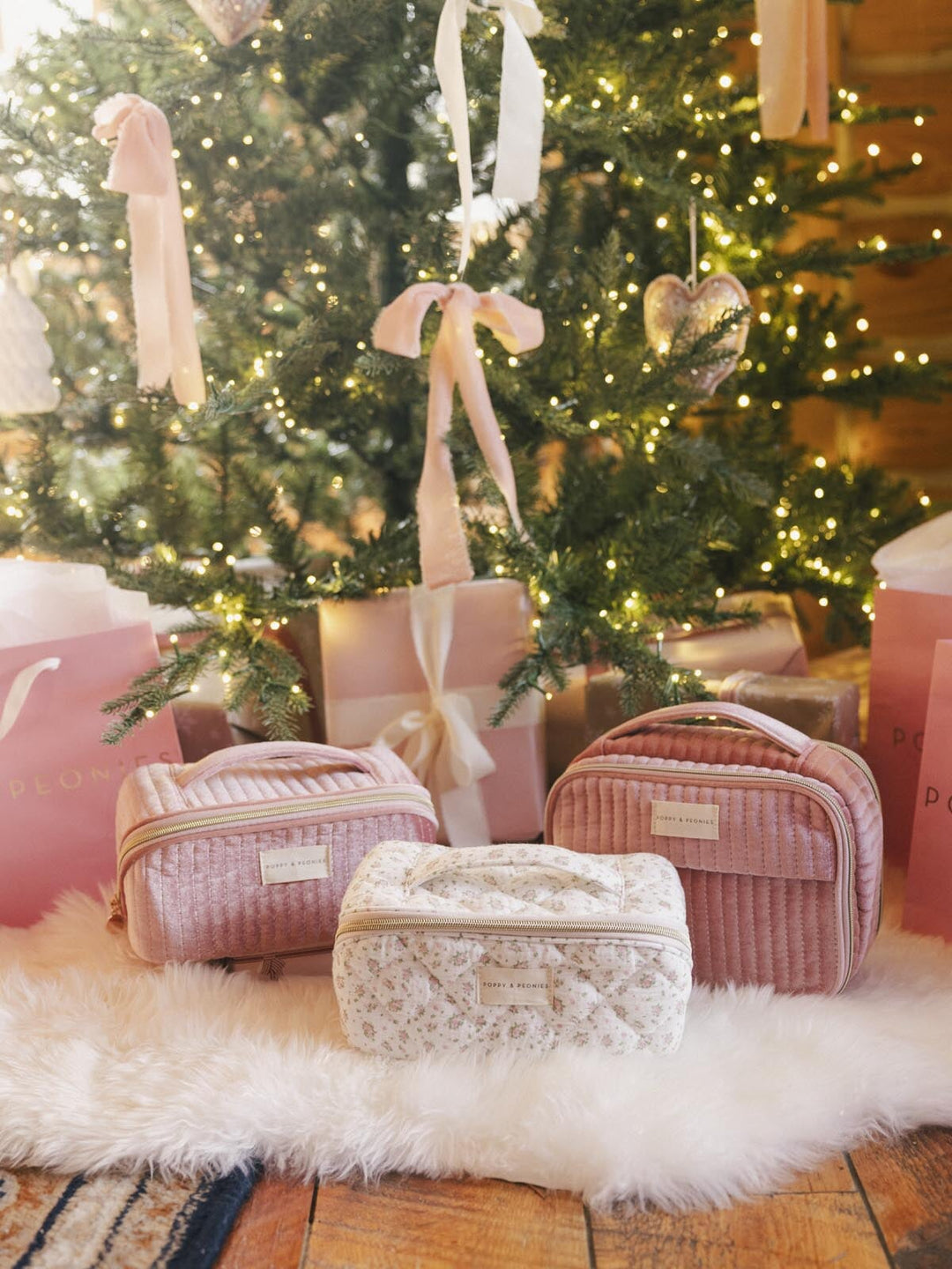 Three cosmetic cases and pink gift bags under a Christmas tree