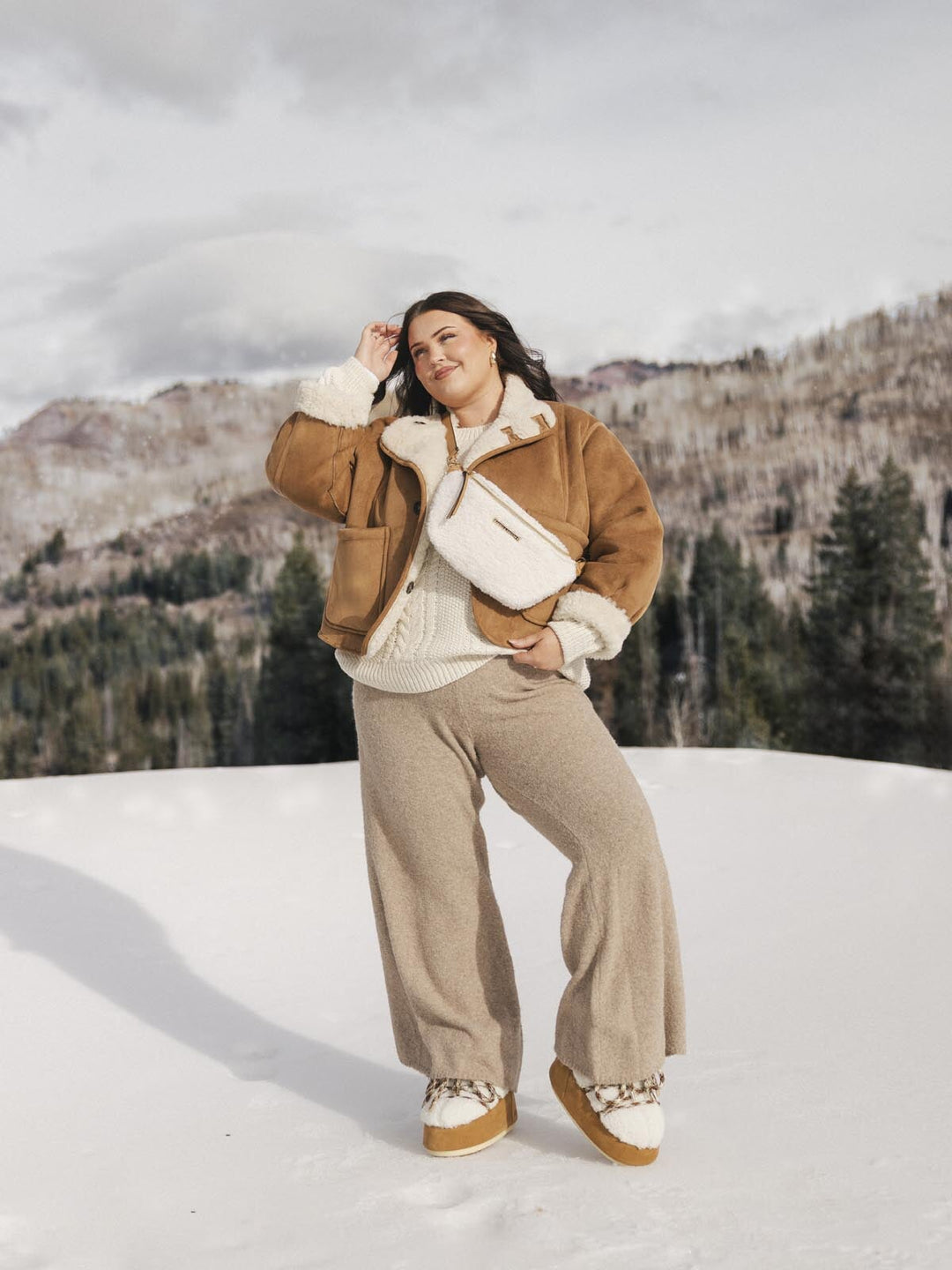 Person wearing a cream faux fur crossbody bag standing in the snow.