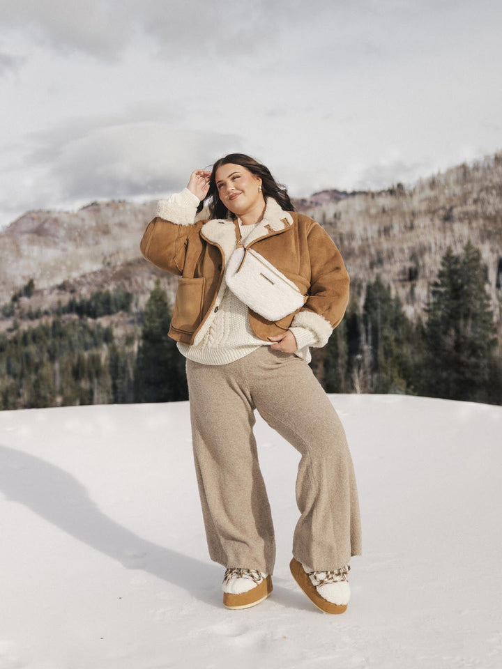 Person wearing a cream faux fur crossbody bag standing in the snow.