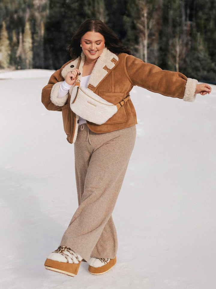 Person wearing a cream faux fur crossbody bag standing in a snowy landscape.