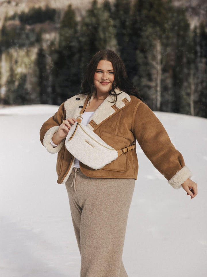 Person wearing a brown jacket and cream faux fur crossbody bag in a snowy landscape.