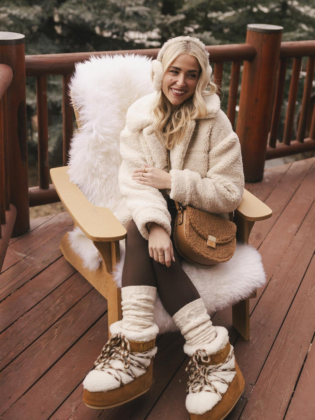 Woman in a fluffy white coat and handbag sitting on a wooden chair outdoors.