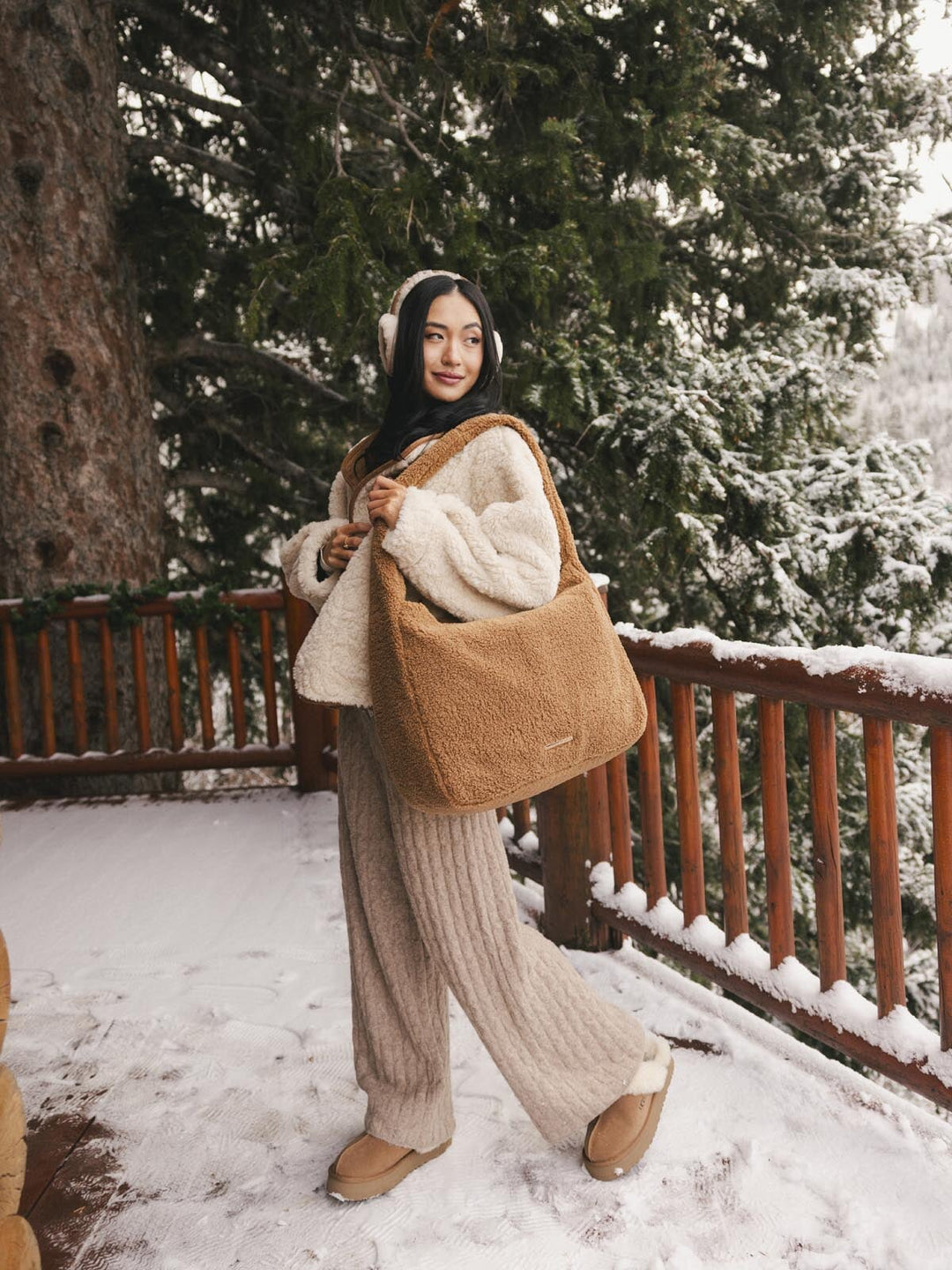 Person in winter clothing holding a brown faux fur bag with snow-covered trees in the background
