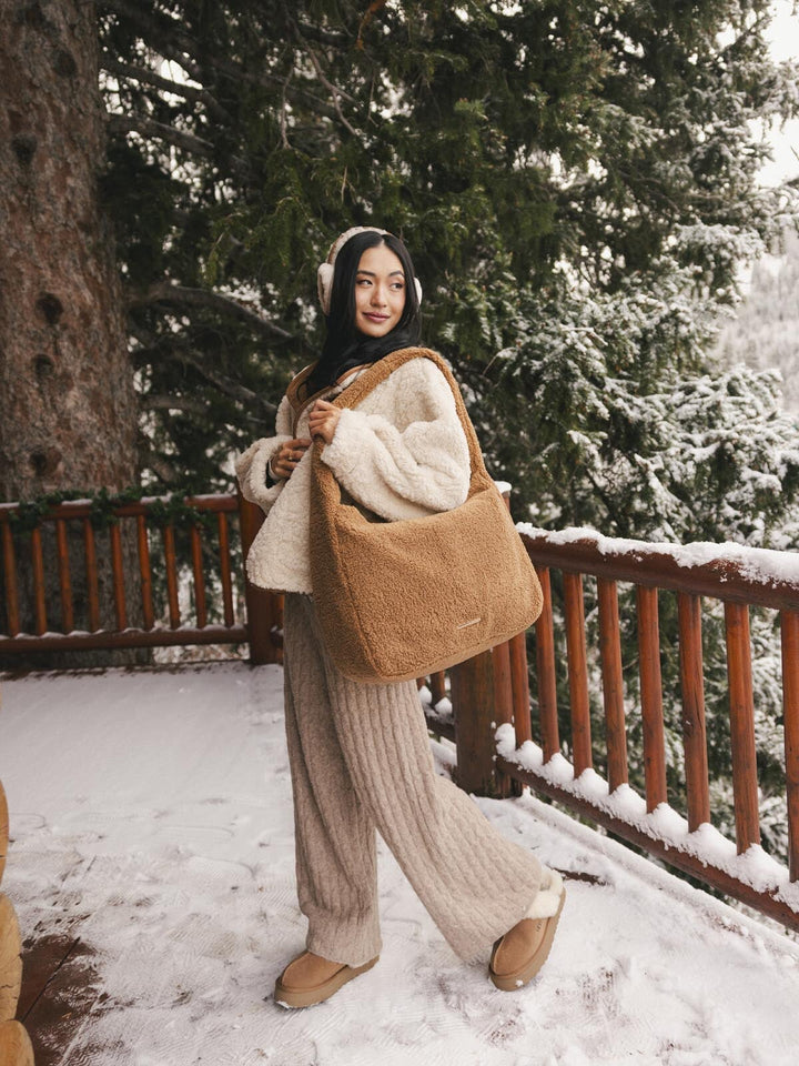 Person in winter clothing holding a brown faux fur bag with snow-covered trees in the background